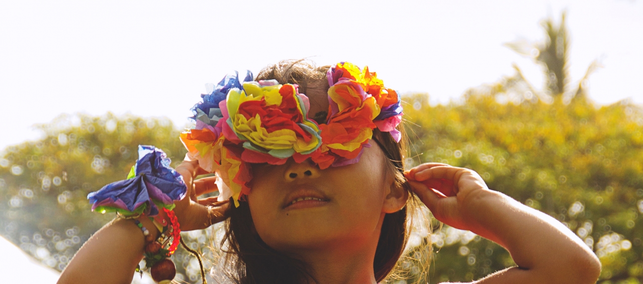 A young girl is looking up at the sky and wears fresh flowers on her wrist and head.
