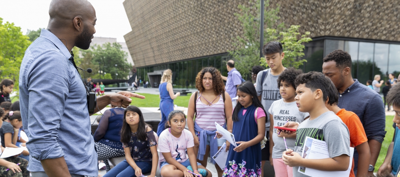 A museum educator engages students outside the National Museum of African American History and Culture 
