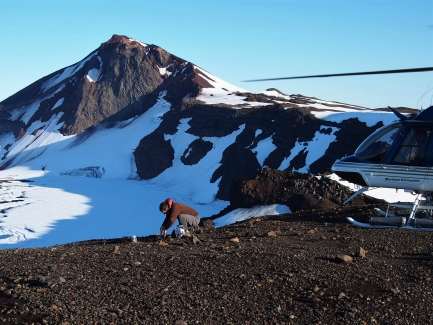 Man kneels next to a volcano while collecting ash samples