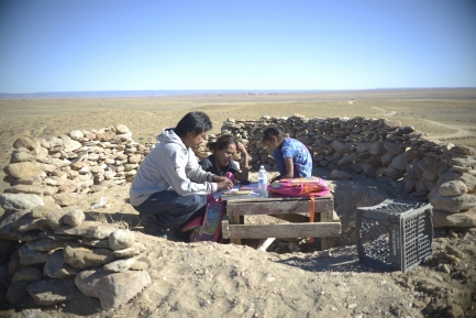 Three people sit in a makeshift classroom outdoors.