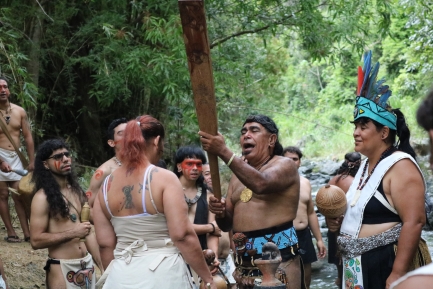 People in traditional dress at naming ceremony; priest touching woman with stick