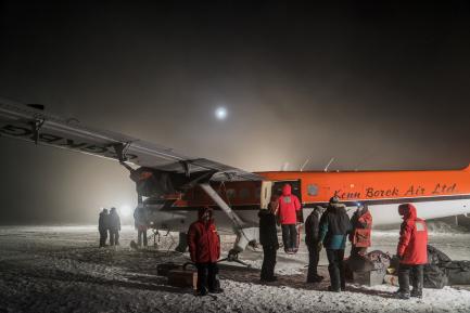 crew in orange parkas loading small plane at night
