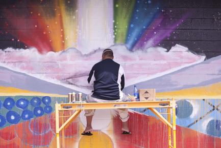 Still image from film Mele Murals showing artist working on rainbow mural