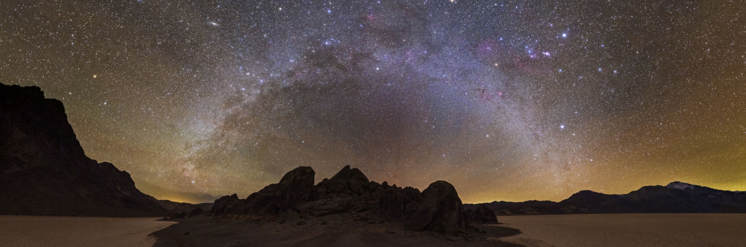 A photo highlighting stars in a twinkling Milky Way with rocky outcroppings below.
