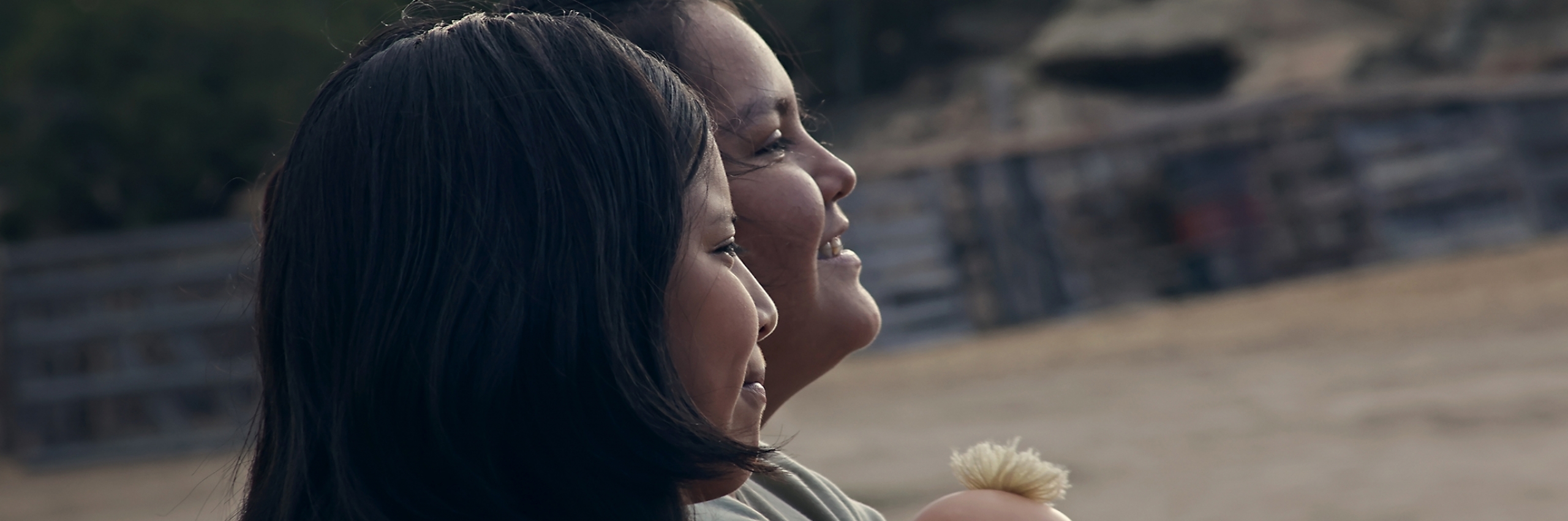 A still from the film Frybread of two women staring in the distance, one holds a doll.