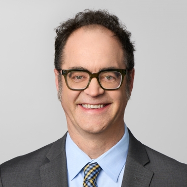 Man wearing a suit and glasses smiles for a headshot