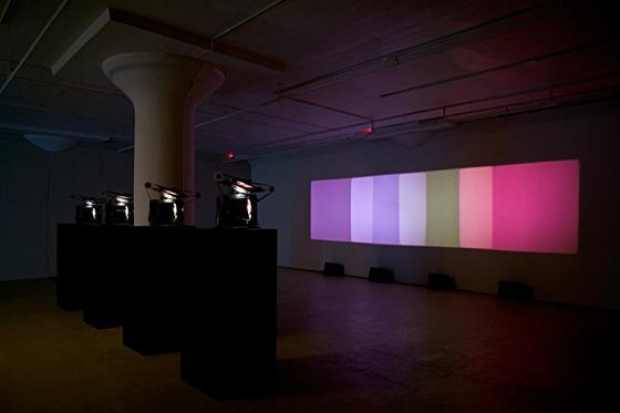Four film projectors in a darkened gallery project color fields in a superimposed fashion.