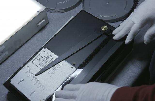 Gloved hands using device to measure film strip